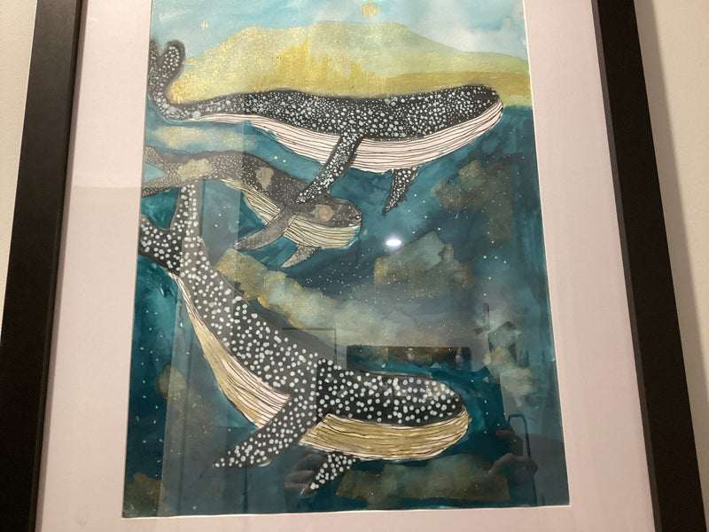 A framed artwork showing three whale sharks swimming through a teal and gold ocean, decorated with white and light blue spots. The background features swirling ink in shades of blue and gold, giving the scene a magical, dreamy quality.