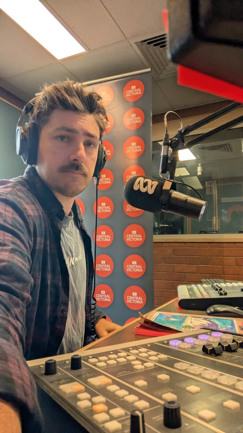 Ryan in the ABC Central Victoria studio with headphones on, a kid's drawing on the desk in front of him