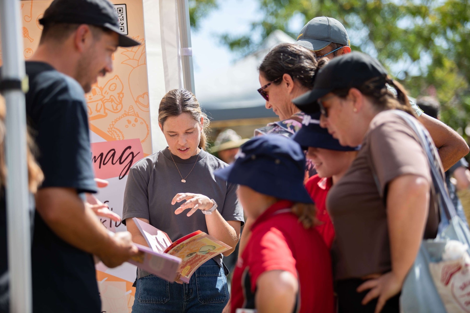 Tam showing an issue of theINmag to families at a market stall