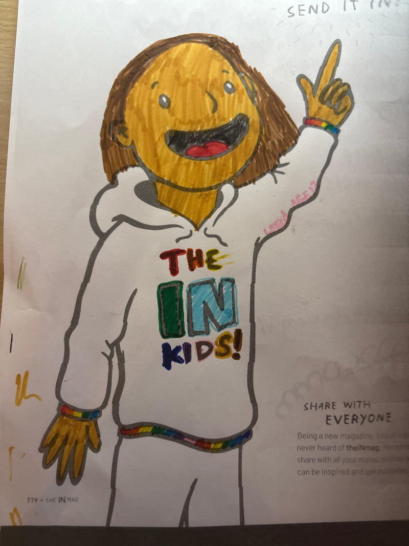 A coloured drawing of a cartoon-style character with a round orange face and brown hair, wearing a white hoodie that reads 'The IN Kids!' in colourful letters. The character is smiling and holding up a peace sign, with rainbow-coloured bracelets on both wrists.