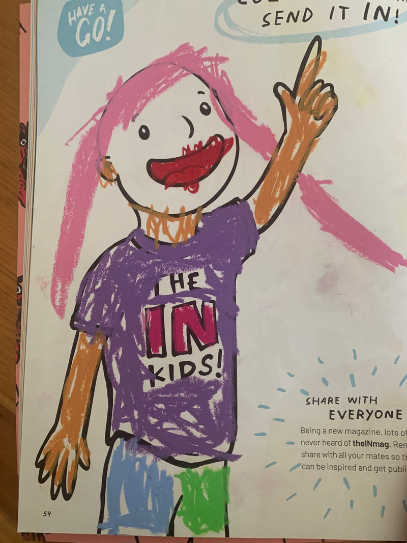 A child's colourful crayon drawing of a cartoon figure with pink hair wearing a purple 'The IN Kids' t-shirt, with arms and face coloured in orange and red. The drawing appears to be a coloured-in version of a magazine mascot character, with enthusiastic scribbled colouring throughout.