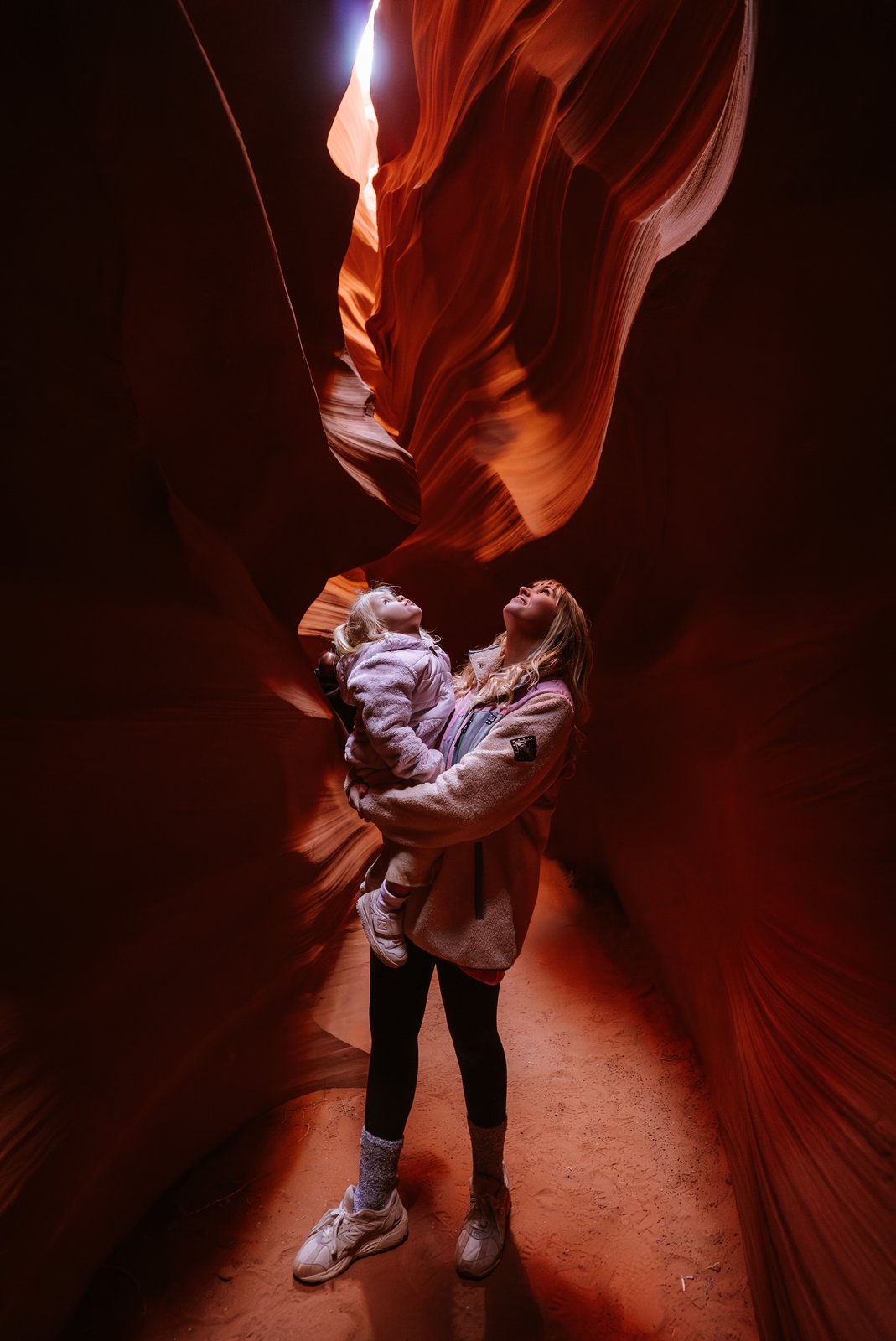 A mum holds a child inside the glowing orange walls of Antelope Canyon.