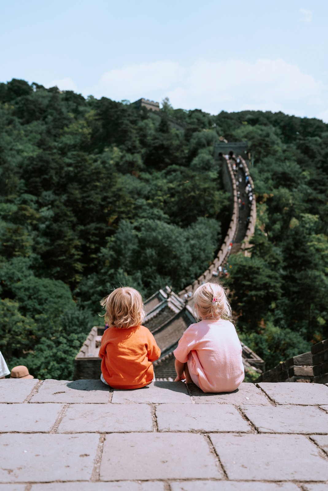Two kids sit looking out along the Great Wall of China.