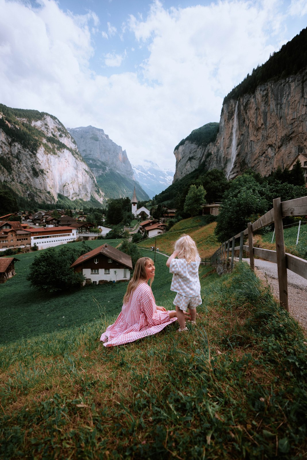 A girl in a pink dress runs through a green alpine valley in the Swiss Alps.