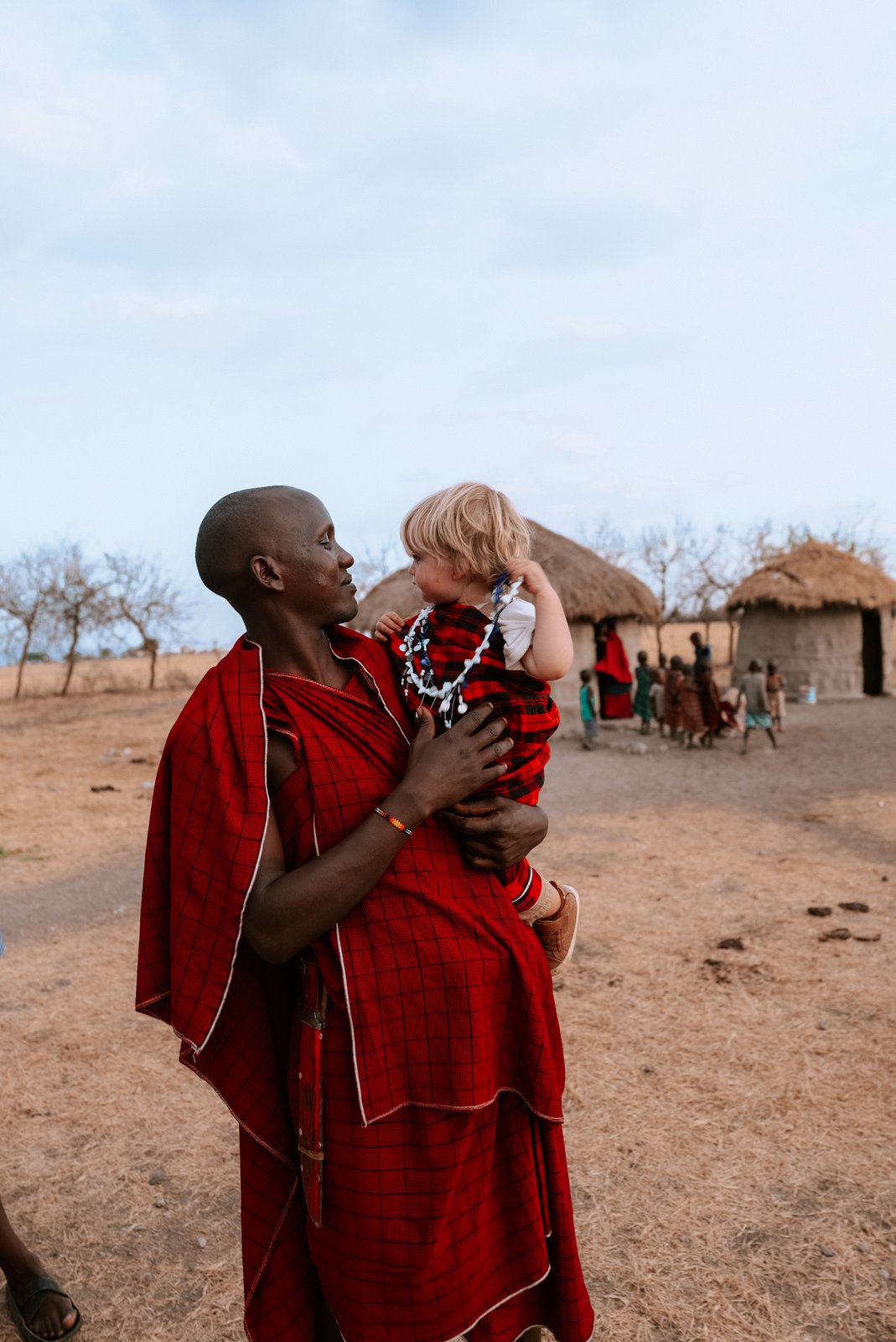 A Maasai man in red robes holds one of the children.