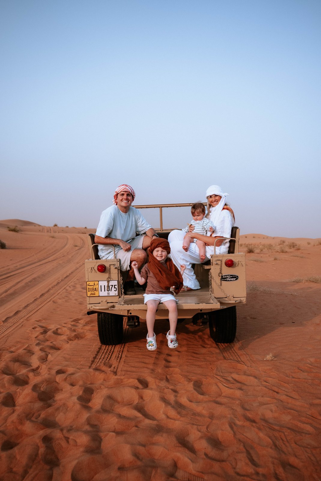 The family on the back of a vehicle among orange desert dunes.